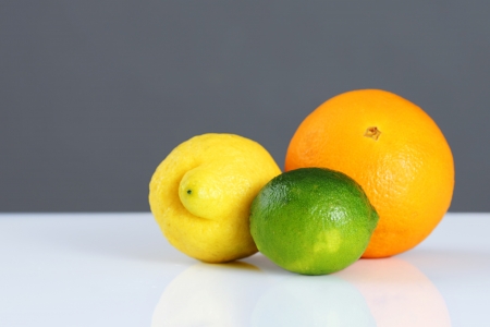 Beautiful studio still life of whole citrus fruits, orange, lemon and lime on white table and grey wall, perfect background for nutrition, diet, healthy eating, organic or other food concept.の写真素材