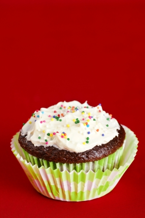 Delicious chocolate cupcake topped with  cream cheese frosting and colorful candy over red background for copy space.の写真素材