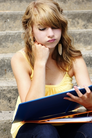 Unhappy or frustrated young blond teenager girl going back to school or looking at her homework in a binder.の写真素材