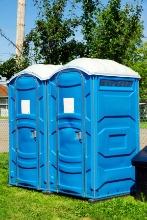 Two portable toilet or loo in blue plastic at a park public event or concert, with white sign on door ready for text.の写真素材