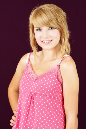 Portrait of cute and innocent yound blond teenager girl smiling, studio shot over deep pink or purple background.の写真素材