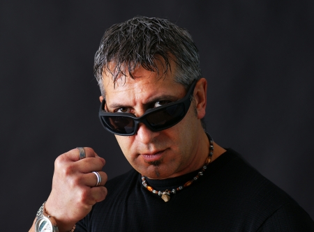Angry tough guy or criminal with dark biker sun glasses staring at viewer and threatenig him with his closed fist.の写真素材