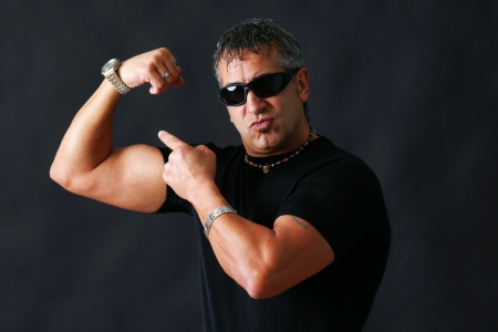 Tough guy with dark glasses, could be criminal, showing his big bicep muscle has an intimidation tactik, studio shot over black.の写真素材