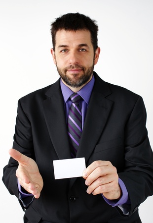 Middle aged man smiling while presenting his hand to meet a colleague while holding a blank business card, great business concept.の写真素材