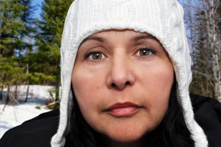 Portrait of middle aged caucasian woman enjoying winter time outdoors in nature, keeping warm with her white wool hat and black coat.の写真素材