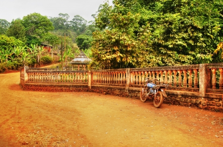 Old motorcycle against fence, African dirt road landscapeの写真素材