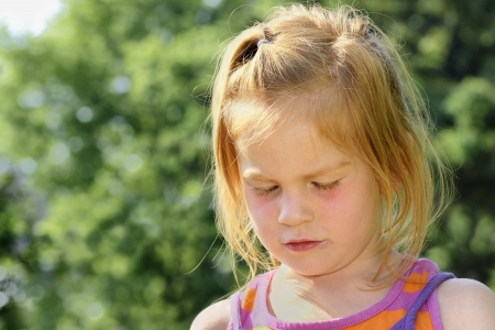 Sad or crying red haired little girl looking down.の写真素材