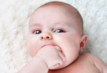 Little baby soothing her itchy gums by putting her thumb and hand in her mouthの写真素材