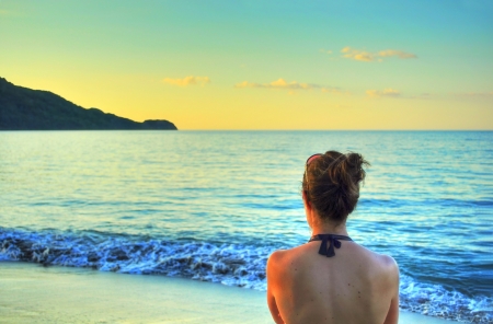 Young woman's back, enjoying the sunset over the sea at the beach in Costa Rica, cyan and yellow tonesの写真素材