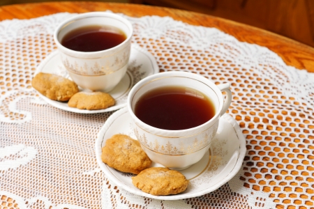Two full tea cups with cookies, vintage decor with antique tea set with gold, lace and oak tableの写真素材