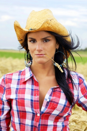 Portrait of a pretty dark hair cowgirl with straw hat standing in a ripe wheat fieldの写真素材