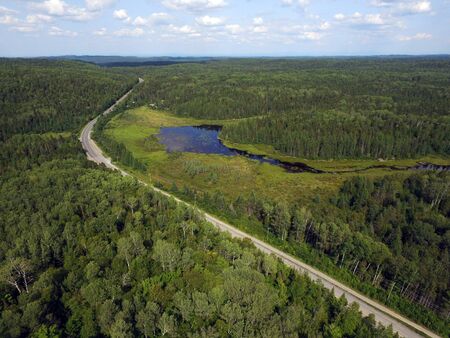 Aerial view of a road going through forest and mountains with bog or marsh, Quebec, Canadaの写真素材