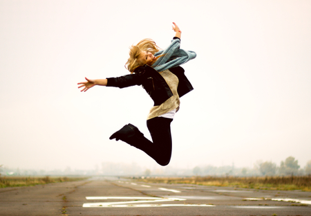 Beautiful happy young woman jumping high in the air, against background of runwayの写真素材