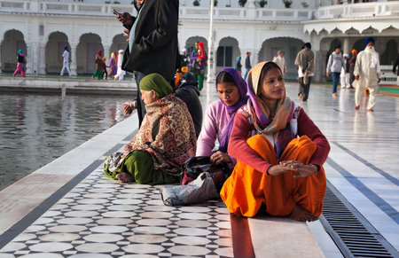 AMRITSAR, INDIA, DEC - 7, 2014: Unidentified Indian women sitting near the lake at Golden Temple (Harmandir Sahib also Darbar Sahib). Golden Temple is the holiest Sikh gurdwara located in the city of Amritsar, Punjab, India.のeditorial素材