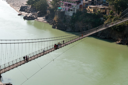 RISHIKESH, INDIA - DEC 9, 2014: Laxman Jhula bridge over Ganges river.  People crossing footbridge. Rishikesh is  World Capital of Yoga,  has numerous yoga centres that also attract touristsのeditorial素材