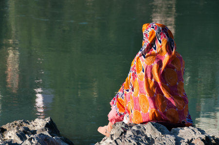 RISHIKESH, INDIA - DEC 10, 2014: Unidentified Indian woman in sari sits on a rock at the River Ganga. Rishikesh is  World Capital of Yoga,  has numerous yoga centres that also attract touristsのeditorial素材