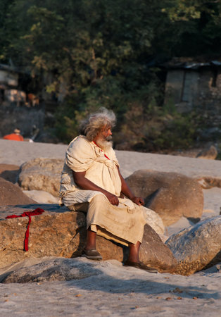 RISHIKESH, INDIA - DEC 10, 2014: Unidentified Indian man sits on rock at the beach near River Ganga. Rishikesh is  World Capital of Yoga,  has numerous yoga centres that also attract touristsのeditorial素材