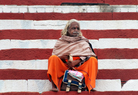 VARANASI, INDIA - DEC 23, 2014: Unidentified Indian Sadhu sits on the steps of the Kedar ghat near...