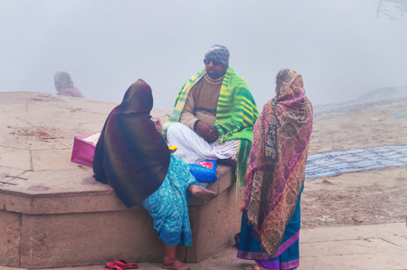 VARANASI, INDIA - DEC 24, 2014: Unidentified Group of Indian people on the ghat near sacred river Ganges at cold foggy winter morning. Varanasi. Uttar Pradeshのeditorial素材
