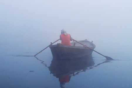 VARANASI, INDIA - DEC 24, 2014: Unidentified Indian man sailing on the boat on sacred river Ganges at cold foggy winter morning. Varanasi. Uttar Pradeshのeditorial素材