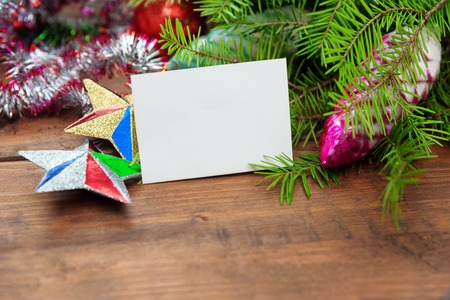 Branch of green fir tree with christmas toys and blank paper on wooden backgroundの写真素材
