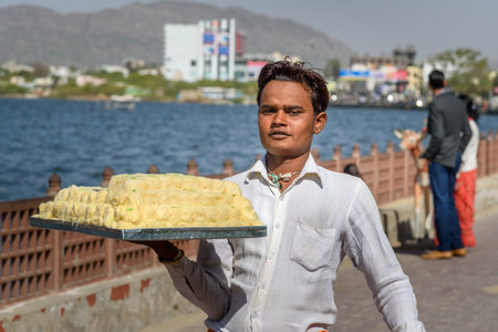 Ajmer, India - February 07, 2019: Indian guy carries sweets on tray for sale on the street in Ajmerのeditorial素材