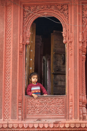 Bikaner, India - February 11, 2019: Indian young girl in wooden carved window in old city of Bikaner. Rajasthanのeditorial素材