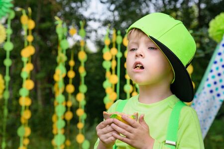 Little boy eating biscuit on colorful background in park in summer dayの写真素材