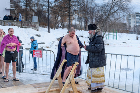 Nizhny Tagil, Russia - January 19, 2019: Priest consecrates the ice hole. Man bathes into cold water of ice-hole. Traditional ice swimming in Orthodox church Holy Epiphany Dayのeditorial素材