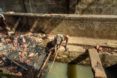 Mumbai, India - February 26, 2019: Indian man cleaning gutter in Dharavi Slum at Mumbai