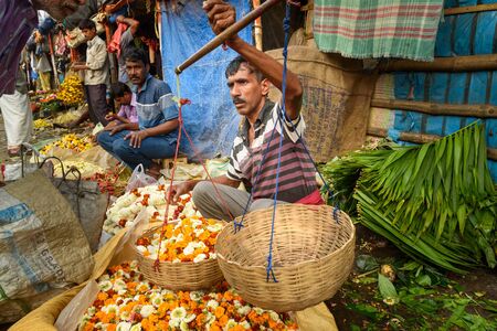 Kolkata, India - March 11, 2019: Indian seller weighs flowers by scales on Flower market at Mallick...