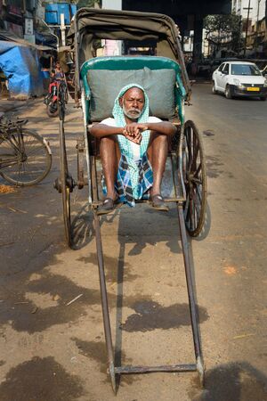 Kolkata, India - March 14, 2019: Indian rickshaw puller sitting on his rickshaw and waiting for...