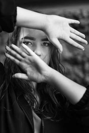 Girl covers her face with her hands and looks through hands. White and black portraitの写真素材