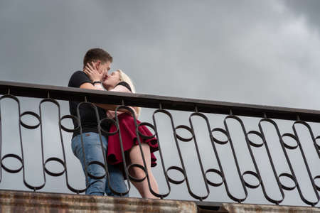 Beautiful loving each other couple is standing and kissing on the bridge on dramatic sky backgroundsの写真素材