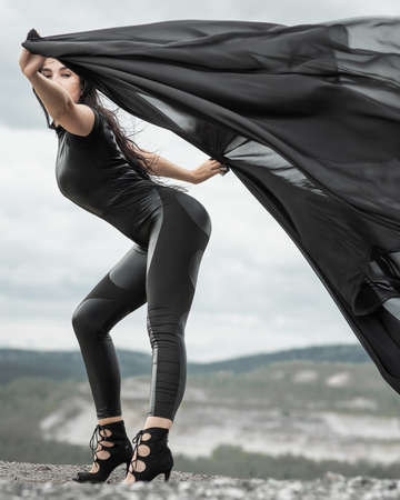 Woman in black overalls dancing with flying fabric outdoorsの写真素材