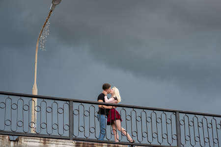 Beautiful loving each other couple is standing and kissing on the bridge on dramatic sky backgroundsの写真素材