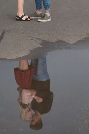 Young couple in love kissing reflected in puddle on the streetの写真素材