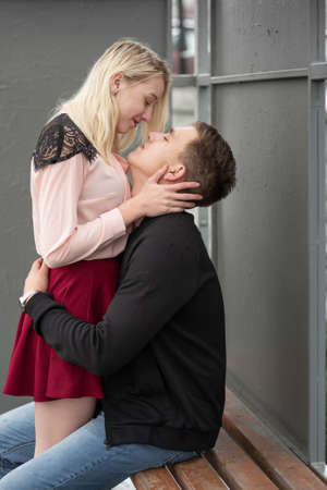 Young couple kissing sitting at bench at bus stop in rainの写真素材