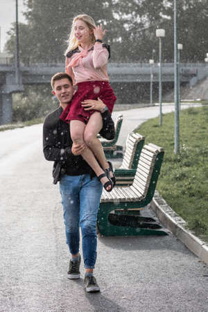 Strong man carrying his woman on shoulder in the city street on rain