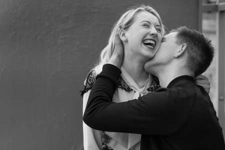 Young couple kissing sitting at bench at bus stop in rainの写真素材