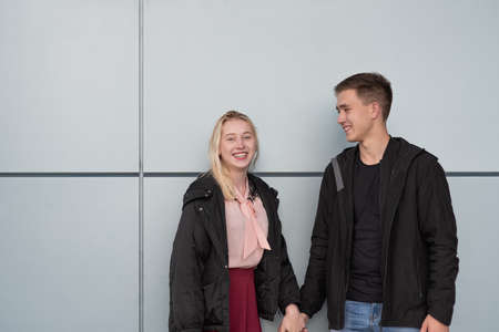 Happy young couple standing near gray wall in the street