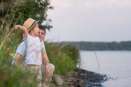Father with son throw pebbles into the water in summer eveningの写真素材