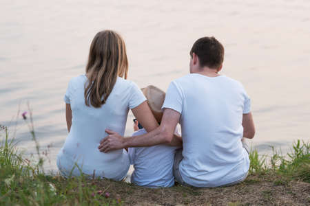 Family sitting near the lake on nature in summer eveningの写真素材