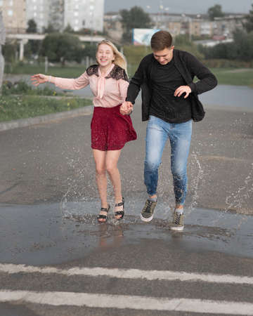 Young couple in love holding hands run on street with splashing in puddlesの写真素材