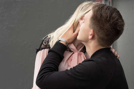 Young couple kissing sitting at bench at bus stop in rainの写真素材