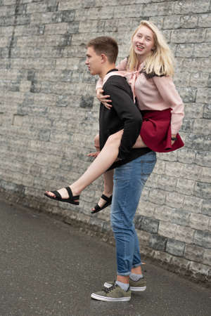 Happy man giving piggyback ride to his girlfriend and laughing near gray wall on the streetの写真素材