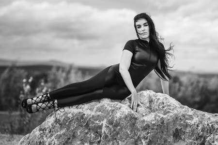 Elegant woman in black overalls is lying on gray big stone. Black and whiteの写真素材