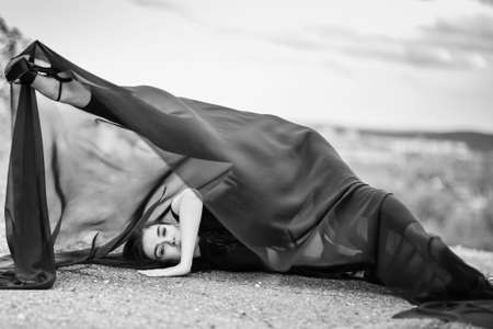 Woman in black overalls dancing with flying fabric outdoors. Black and white