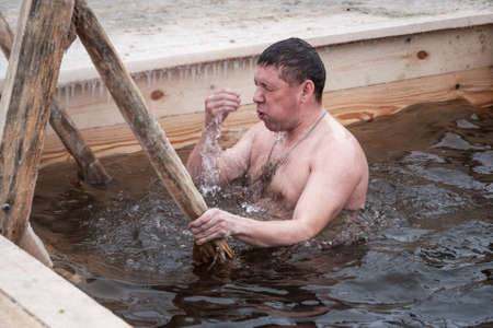Nizhny Tagil, Russia - January 19, 2020: Man bathes into cold water of ice-hole on Epiphany day....