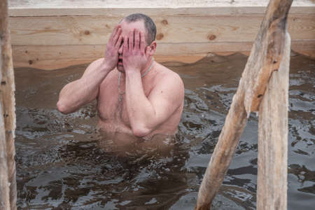 Nizhny Tagil, Russia - January 19, 2020: Man bathes into cold water of ice-hole on Epiphany day. Traditional ice swimming in Orthodox church Holy Epiphany Dayのeditorial素材